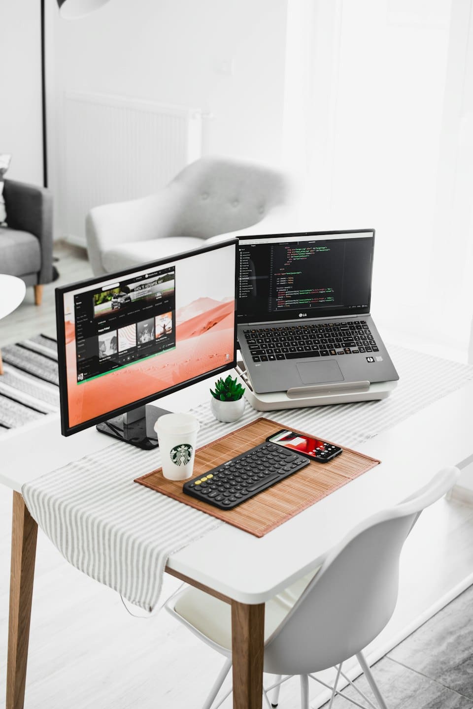 Modern home office with laptop, external monitor showing code, and desk accessories.